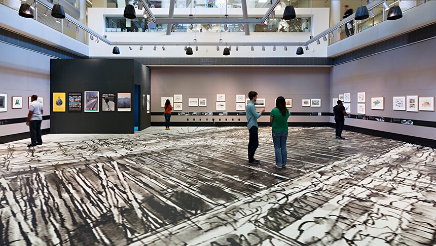 People looking at a large room with art on the floor
