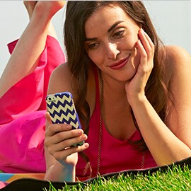  A smiling woman laying on grass looking at her mobile phone.