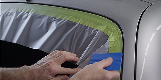 person putting a blue and grey plastic film on a car
