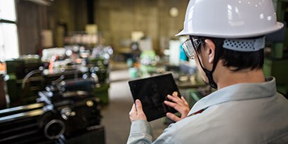 Image of a man using a tablet with a privacy screen to oversee production in an industrial plant.
