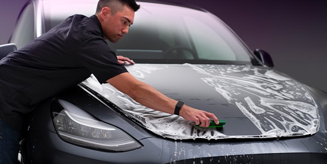 man applying soapy paint protection film to hood of car
