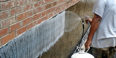 Worker spraying 3M™ HoldFast 70 Spray Adhesive on a below-grade wall before attaching waterproofing or insulation
