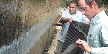 Workers using spray adhesive to install below-grade waterproofing
