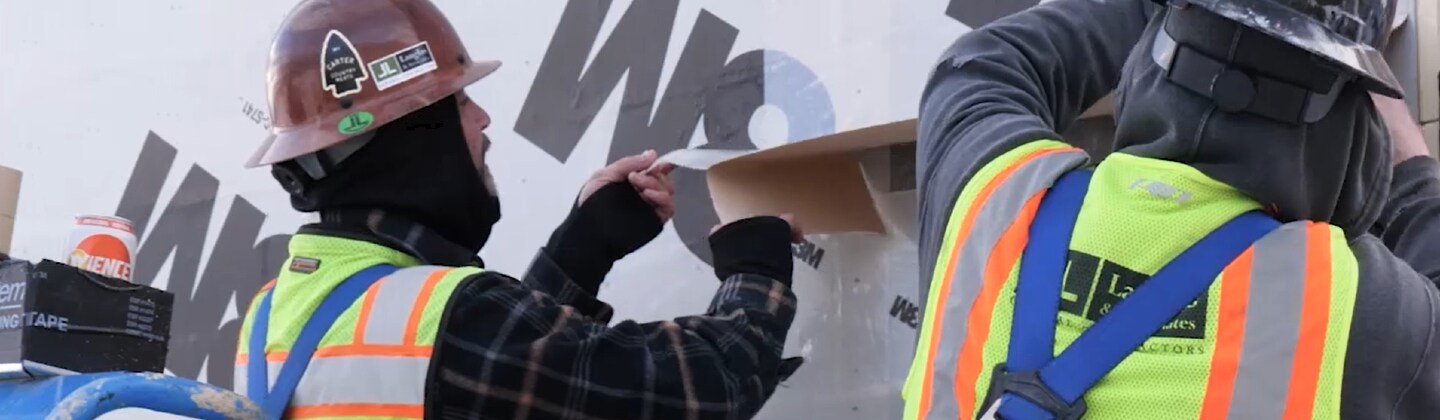 Video still of workers dressed for cold weather removing the liner and applying a 3M™ Air Barrier
