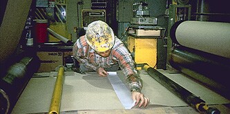 A man in construction wear is aligning film on a work station
