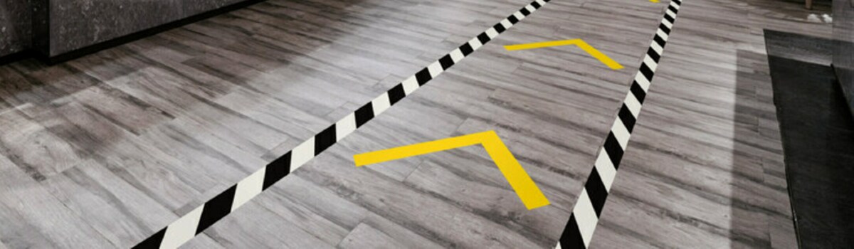 Image of a floor with traffic lane marked with black-and-white stripe tape and traffic direction marked with yellow tape
