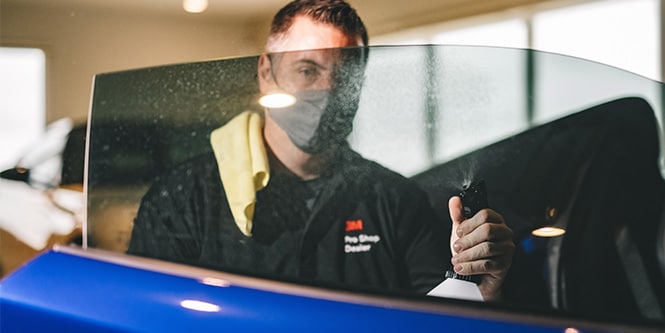 man spraying water on inside of car window tint
