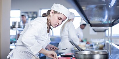 person in chef's uniform looking at a spoon
