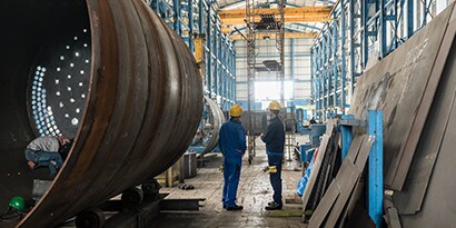 Image of two workers on a factory floor while a third works inside a large round metal cylinder
