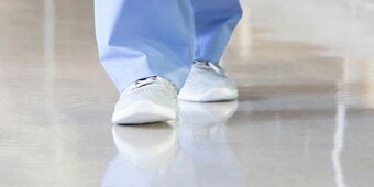 Image of a person in disposable paper pants and booties walking toward the camera over a clean floor
