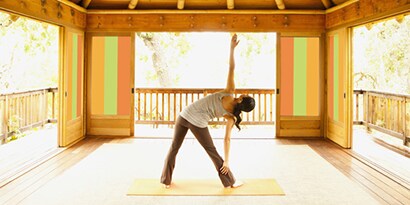 A woman stretching in an all-seasons patio with the doors open and windows covered in orange and green vertical stripes using 3M graphic translucent film.
