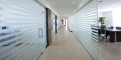 A private property hallway with glass walls that have 3M frosted privacy wall wrap strips on them.
