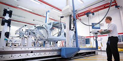 Image of a man at a computer station overseeing the manufacture of a car.
