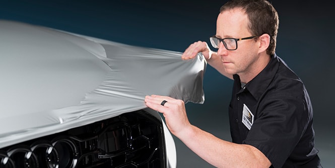 Man stretching wrap film over front of car
