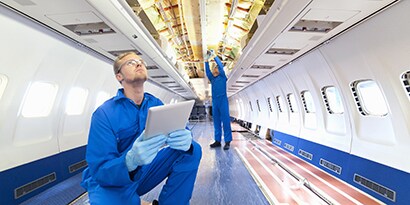 Image of workers using a tablet to help assemble the interior of a commercial plane.
