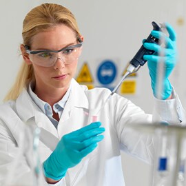 woman wearing  a lab coat and gloves transferring liquid using a pipette