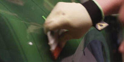 A man applying 3M IJ180mC print wrap film on the side of a car with a squeegie tool.
