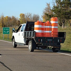 A truck carries orange and white plastic safety drums for highway construction.