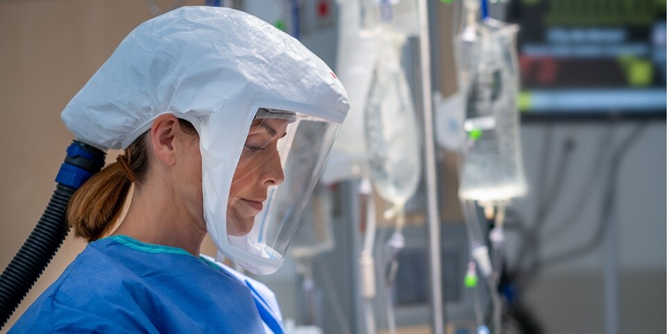 health care worker in a protective respirator and goggles conversing with patient
