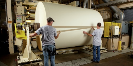 대형 용지 롤 끝부분에 테이프를 감고 있는 작업자 이미지
