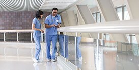 Image of two medical professionals consulting near a walkway railing
