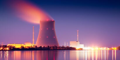 A nuclear power plant in the distance with a body of water in front of it.
