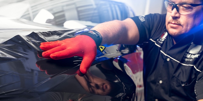 man with red glove applying wrap film to side of car
