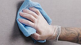 a glove over a hand, holding a cleaning cloth and wiping down a wall with a matte finish.