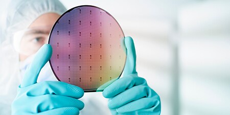 Person in clean room holding a silicon wafer in gloved hands
